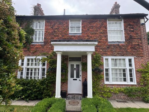 Traditional brick house with white windows and a front porch, surrounded by greenery.